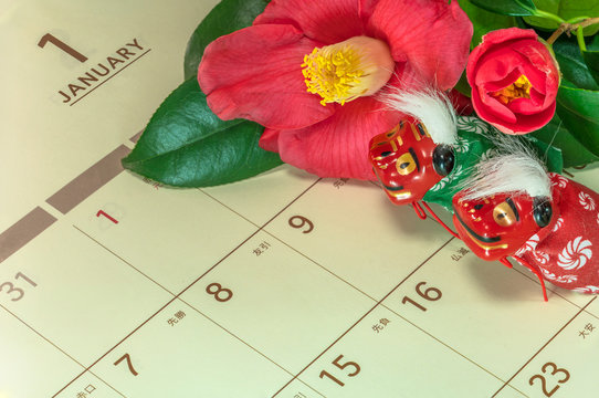 Japanese greeting card with Tsubaki flower called also the rose of winter and cute Japanese Folklore animals figurines of two lions Shishimai on a Japanese calendar open on January page.