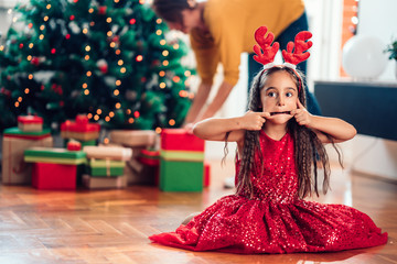 Little girl sitting on the floor and making funny faces for Christmas