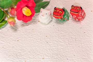 A Japanese greeting card with a Tsubaki flower and three Folklore animals figurines depicting two Shishimai lion and a cute rat figurine for the 2020 year of the mouse on a white crumpled paper