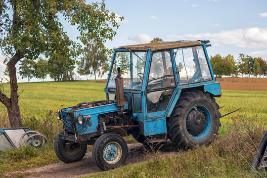 old blue tractor parked at field, sunny autumn day