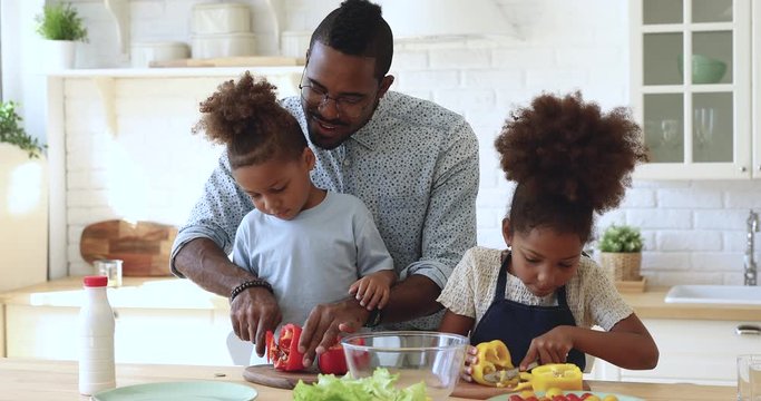 African father teaching son daughter cutting vegetable salad in kitchen