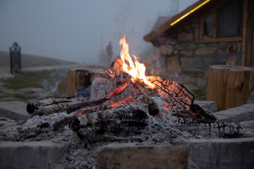The dying fir.Thick smoke over the fire, in the background the stone wall of the house and the fog.