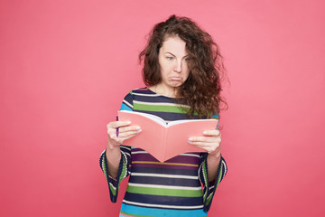 Portrait  of surprised attractive brunette young European woman with scared face expression, afraid of something, interrupts from reading, models against pink studio wall background with copy space.