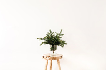 Bouquet of fir-tree branches on solid wooden stool on white background. Minimal Christmas, New Year composition.