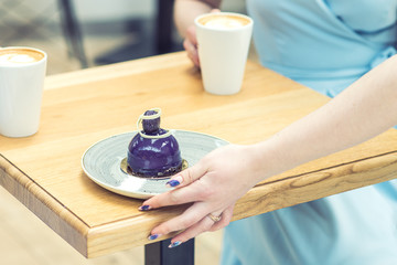 The hand of the waiter puts the piece of cake on the table at cafe. Showing the hand of the waiter.