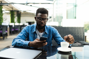 Young black man outside at cafe looking at his smartphone