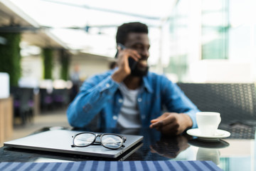 Smiling young african man drinking coffee and talking on mobile phone while sitting in cafe