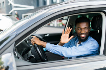 Young handsome african man wave greetings to someone while driving his car