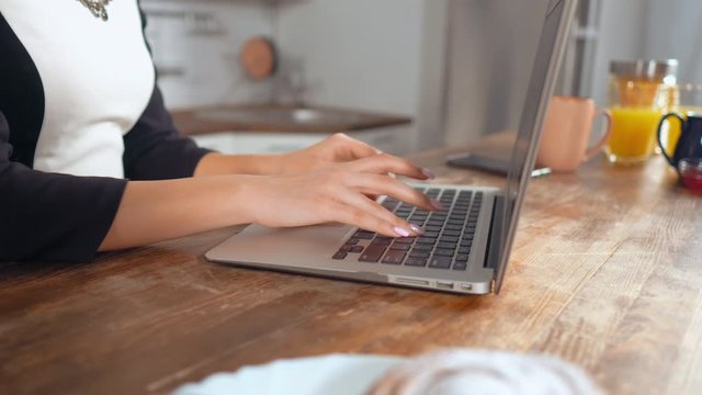 b roll detail woman working in flat typing on laptop keyboard chatting online sitting at the table kitchen interior on the desk food for breakfast