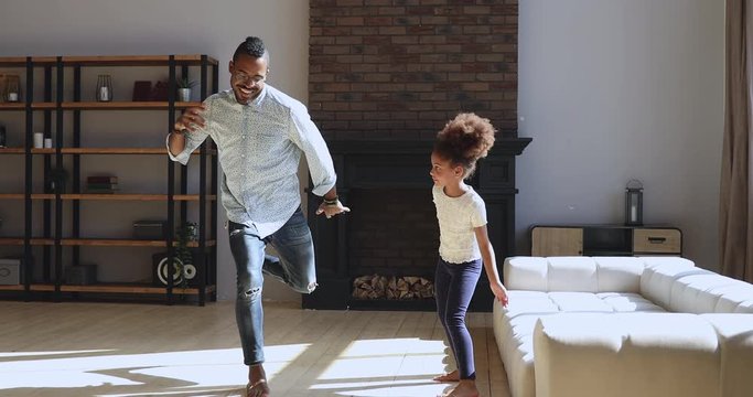 Happy funny african father and daughter dancing in living room
