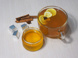 Photo mugs with tea and lemon, jars of honey, cinnamon sticks, star anise and sweets on a light wood background