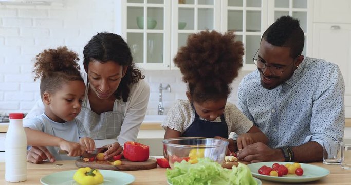 Little african boy and girl helping parents cutting vegetable salad