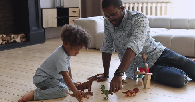 Happy american dad and small son playing dinosaurs at home