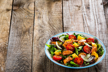Salad with chicken, mango and tomatoes on wooden table