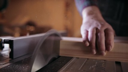 Slow-motion pan of a white man's hand pushing a pretreated piece of timber through a table saw - Powered by Adobe
