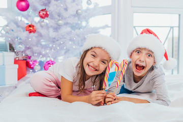 Obraz na płótnie Canvas Shot of extremely excited siblings with candycanes, spending time together in white bedroom on christmas morning.