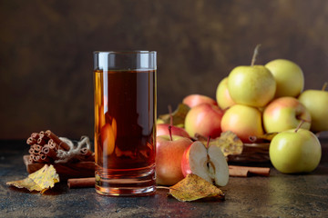 Glass of apple juice with apples and cinnamon sticks.