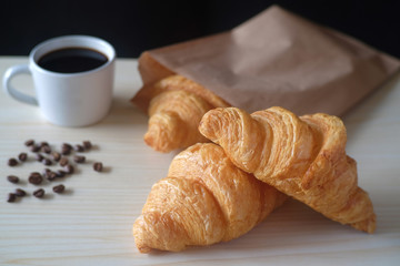 Delicious breakfast with fresh croissants and cup of espresso coffee on wood table.