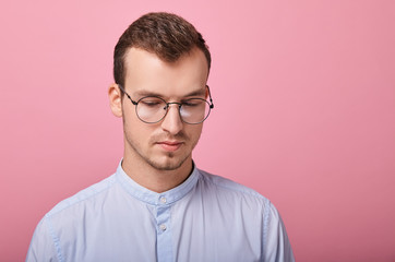 A decent young man in a sky blue shirt and computer glasses stands on a pink background. Student, businessman, employee of the year. Happy. look