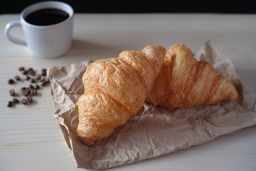 Delicious breakfast with fresh croissants and cup of espresso coffee on wood table.