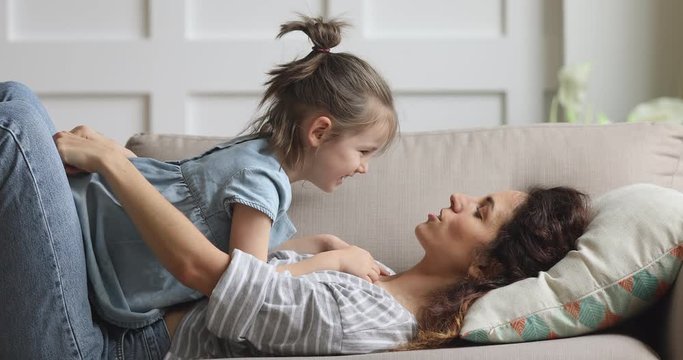 Happy carefree mother and cute child daughter tickling on sofa