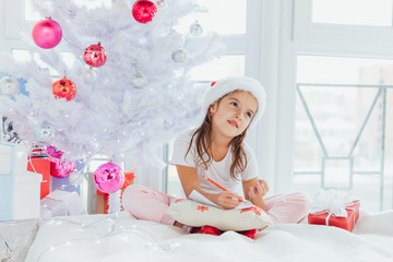 Lovely kid is counting if she've written all her wishes to the letter for santa, looking involved in the process.