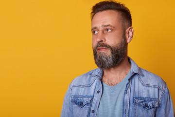 Image of bearded young man with calm facial expression, looking aside, generates ideas, dresses...