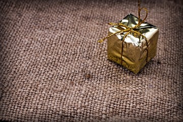 Gold gift box with gold thread on a background of rough fabric