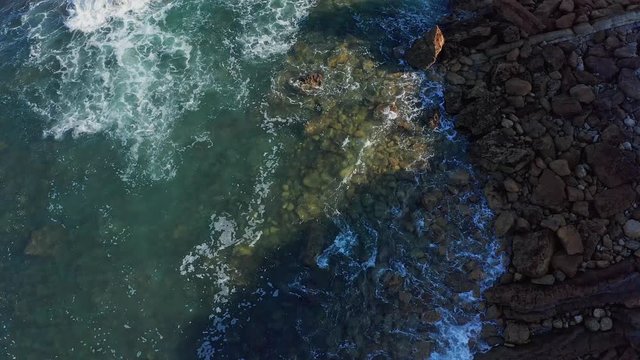 Descending shot over sea waves breaking in the reefs and coast, Cantabrian sea, Spain - drone aerial view