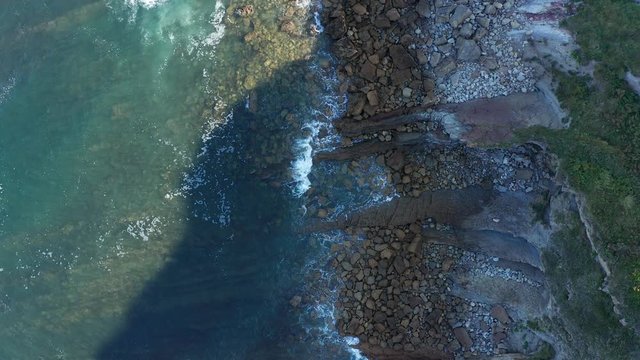 Ascending shot over sea waves breaking in the reefs and coast, Cantabrian sea, Spain - drone aerial view