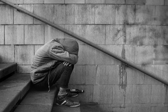 Drunk homeless man covered his face with his hands and sits on the stairs in the underpass, black and white photo.