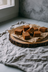 Fresh caramel fudge candies on a wooden plate with copy space in marble background