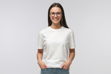 Young smiling woman standing with hands in pockets, wearing blank white tshirt with copy space,...