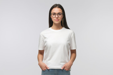 Young smiling woman in white t-shirt and trendy eyeglasses isolated on gray background