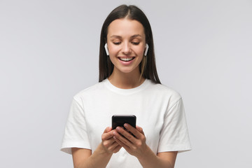 Fototapeta premium Young happy attractive european female with smartphone in hands, isolated on gray background