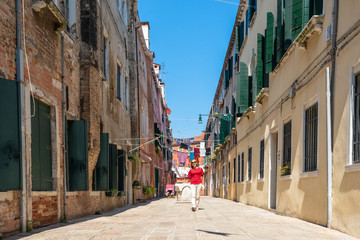 Girl traveler in Venice. A beautiful asian woman in red is walking on Venice street. Laundry is dried on the clotheslines between the houses. Authentic Italian town. Travel Tourism in Europe.