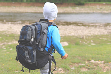 Child boy with big tourist backpack on river and forest background. Active lifestyle, tourism, hiking and  concept.