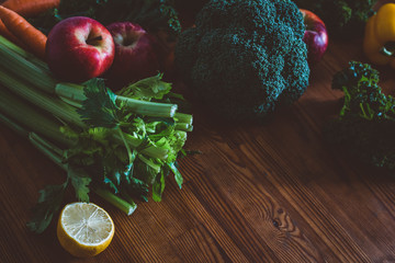 Dark raw food photography: vegetables, fruits and greens on a wooden table