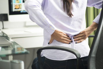Woman sitting at office having back pain due to bad position or having a not ergonomic chair - 296943167