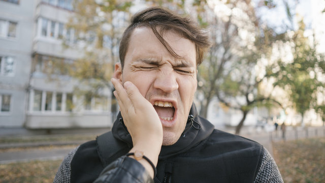 Man getting slapped in the street. Unhappy scared man getting slapped standing into the park