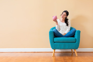 Young woman with a piggy bank sitting in a chair