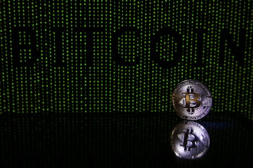 Bitcoin coin with reflection on a black background with a green binary code