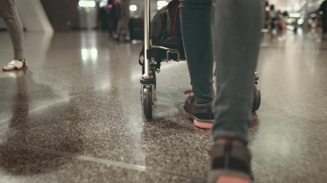 Woman Carry Cart at International Airport Terminal. Tracking Shot of Female Legs in Trainers. Transit Passenger Pulling Trolley Stroll with Baggage to Boarding Gate. Footage Shot in 4K