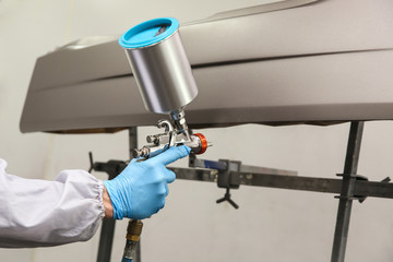 car painter's hand is painting a car detail with spray gun. painting a car part in a spray booth by pulverizer close up