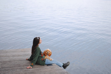 Girl with her dog, English Cocker Spaniel, sitting on the bench near the lake