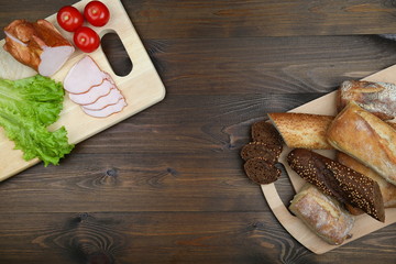 Fototapeta premium culinary background: cutting boards with tomatoes, green salad, chopped ham, bread on a dark wooden surface. sandwich ingredients