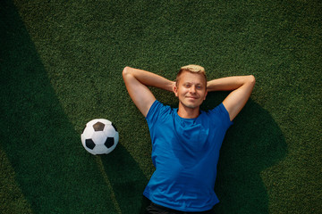 Male soccer player with ball lying on the grass