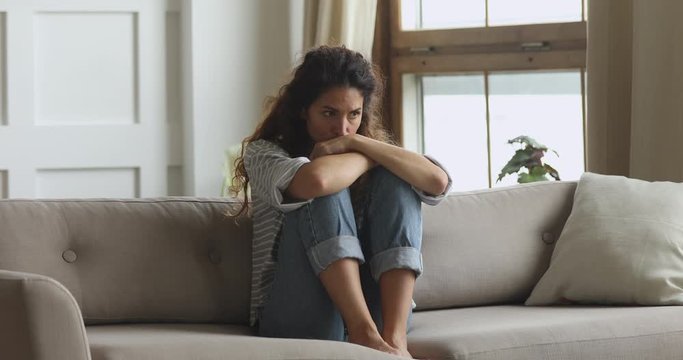 Thoughtful worried young woman sit on couch troubled with problem