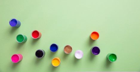 Colorful finger paints set on green color background, top view
