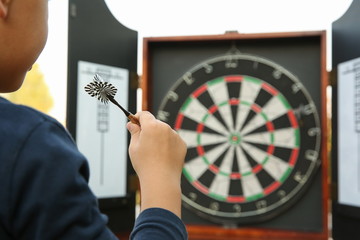 child's hand holds dart on the background of the board for darts